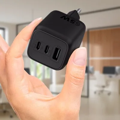 Mão segurando o carregador Intelbras EC 21 Power 65W preto com duas portas USB-C e uma USB-A